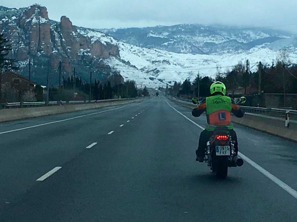 Alumno en moto por carretera con montañas nevadas