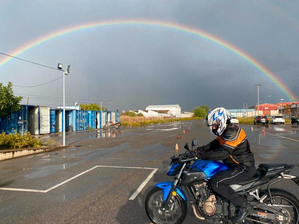 Alumno practicando en moto con arcoíris de fondo